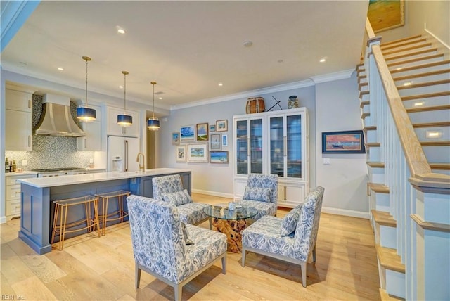 sitting room featuring stairway, baseboards, light wood-style flooring, and ornamental molding