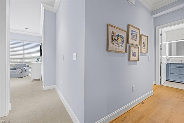 hallway featuring crown molding, light carpet, baseboards, and light wood-type flooring