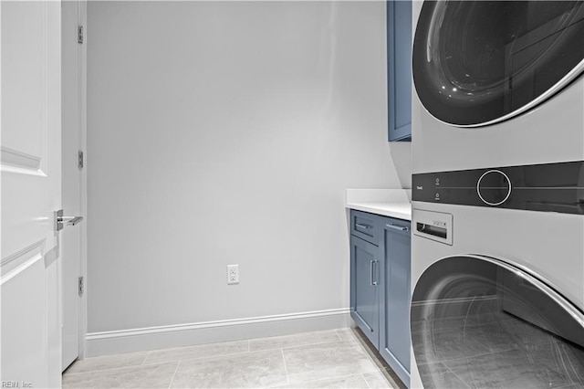 laundry room featuring light tile patterned flooring, cabinet space, baseboards, and stacked washer and dryer