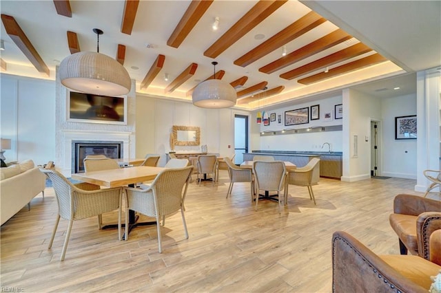 dining room featuring light wood-style flooring, beam ceiling, baseboards, and a glass covered fireplace