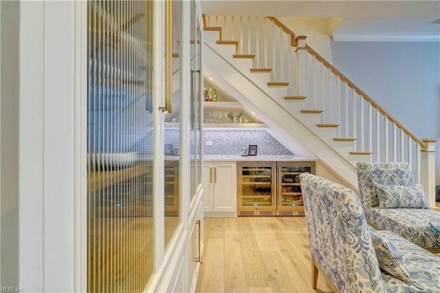 interior space featuring stairway, a bar, light wood-style floors, and ornamental molding