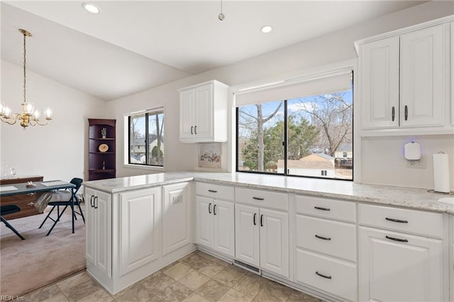 kitchen with lofted ceiling, light stone counters, a notable chandelier, a peninsula, and white cabinetry