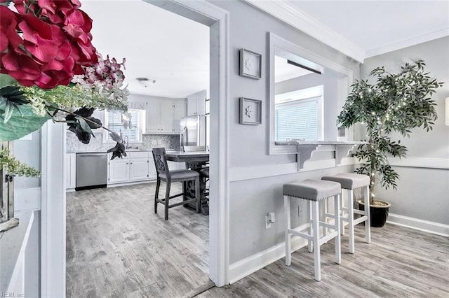 interior space featuring stainless steel appliances, light wood-type flooring, backsplash, and crown molding