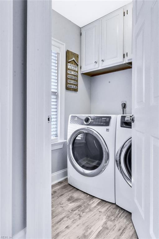 clothes washing area featuring washing machine and dryer, cabinet space, light wood-style flooring, and baseboards