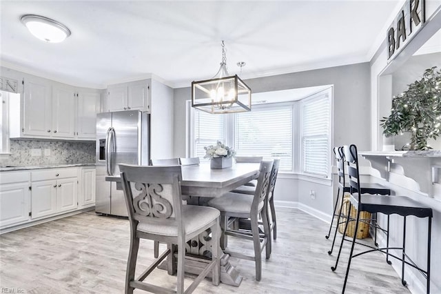 dining room featuring a notable chandelier, light wood-style flooring, baseboards, and crown molding