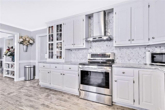 kitchen featuring white cabinets, glass insert cabinets, appliances with stainless steel finishes, ornamental molding, and wall chimney range hood