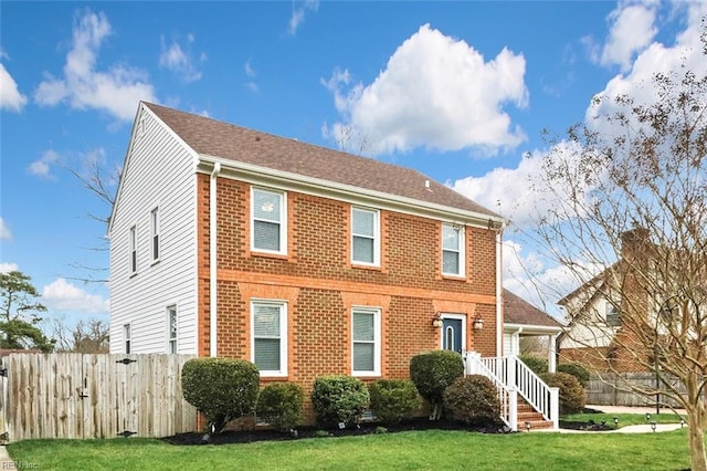 colonial house featuring fence, a front lawn, and brick siding