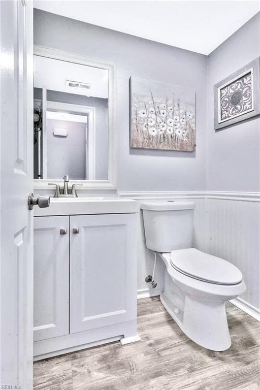 half bathroom featuring toilet, vanity, wood finished floors, and visible vents