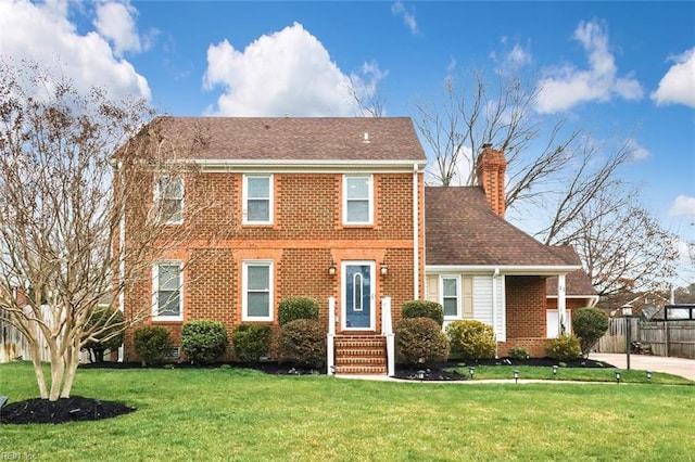 colonial house with brick siding, a chimney, a front yard, and fence