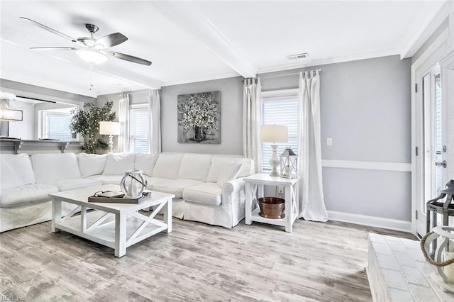 living room featuring wood finished floors, a ceiling fan, baseboards, visible vents, and crown molding