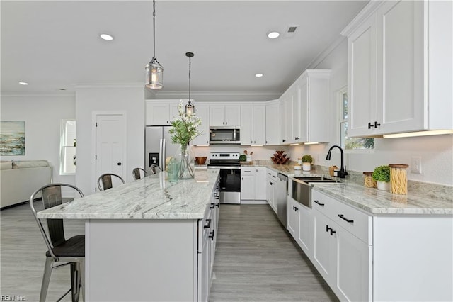 kitchen with ornamental molding, stainless steel appliances, a kitchen bar, white cabinetry, and a sink