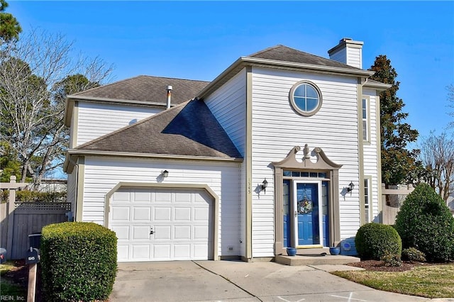 traditional-style home with concrete driveway, a chimney, roof with shingles, an attached garage, and fence