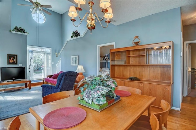 dining space with a textured ceiling, ceiling fan with notable chandelier, a high ceiling, wood finished floors, and baseboards