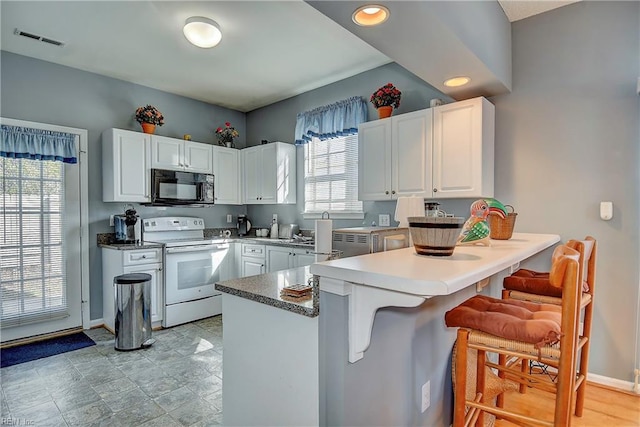 kitchen with black microwave, a peninsula, visible vents, white cabinetry, and white range with electric cooktop