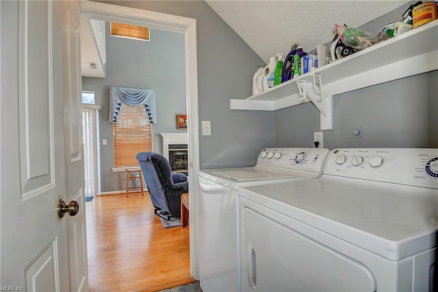 clothes washing area featuring a textured ceiling, washing machine and dryer, laundry area, light wood-type flooring, and a glass covered fireplace