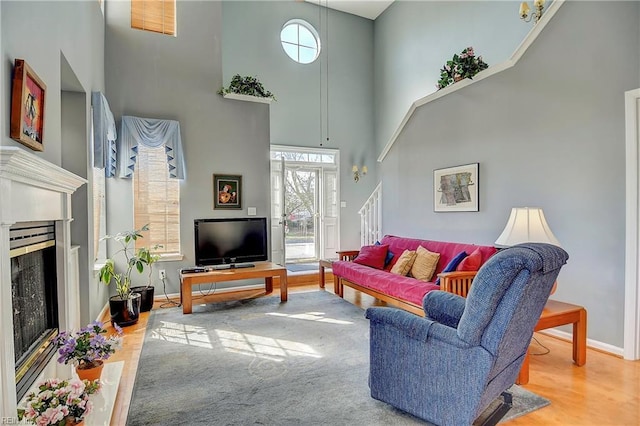 living room featuring a high ceiling, wood finished floors, a fireplace with flush hearth, baseboards, and stairs