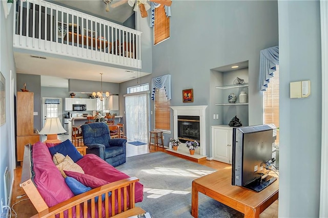 living room featuring visible vents, a high ceiling, ceiling fan with notable chandelier, and a glass covered fireplace