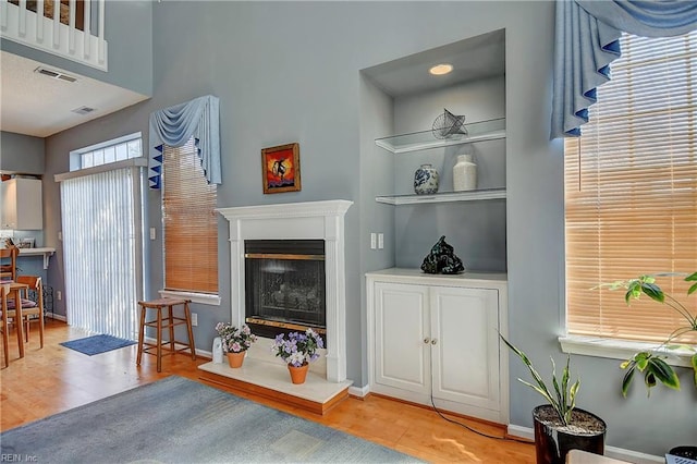 living room with baseboards, visible vents, wood finished floors, and a glass covered fireplace