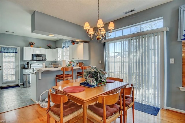 dining room with light wood-type flooring, visible vents, a notable chandelier, and baseboards