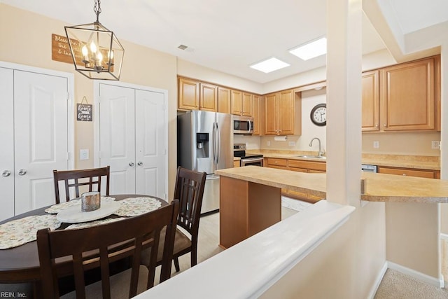 kitchen with baseboards, stainless steel appliances, light countertops, light brown cabinetry, and a sink