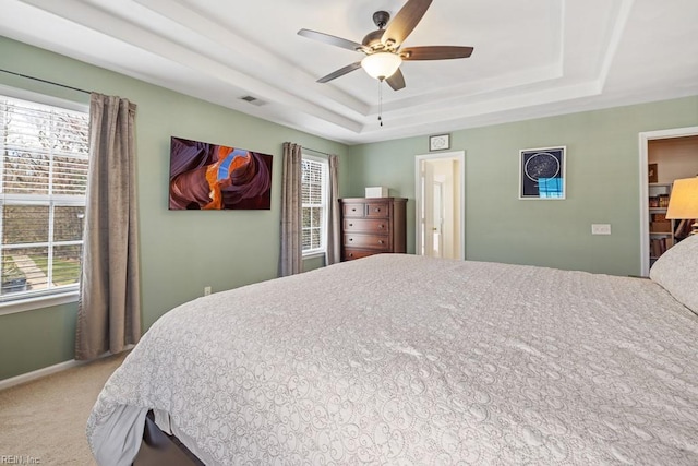 carpeted bedroom with a ceiling fan, a tray ceiling, visible vents, and baseboards