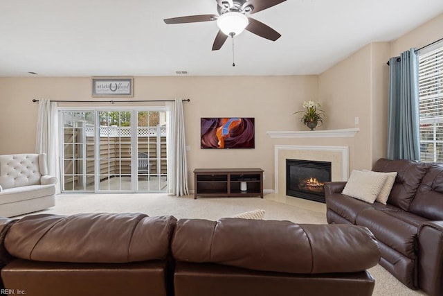 carpeted living room with a ceiling fan, a fireplace with flush hearth, visible vents, and a healthy amount of sunlight