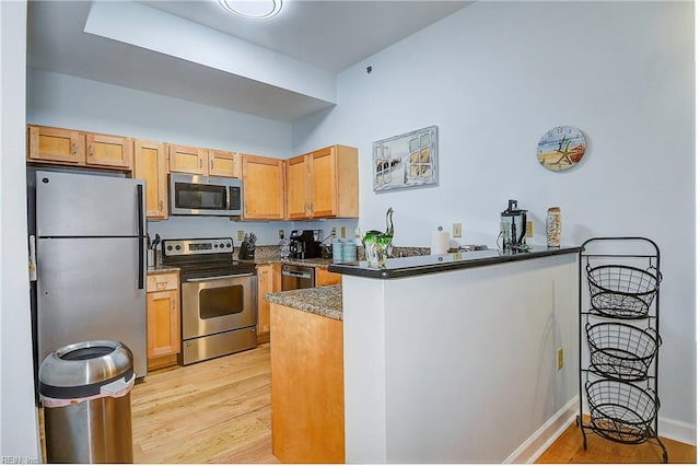 kitchen featuring appliances with stainless steel finishes, light wood-type flooring, a peninsula, and baseboards