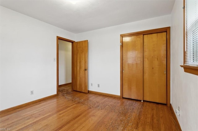 unfurnished bedroom featuring wood finished floors, a closet, and baseboards