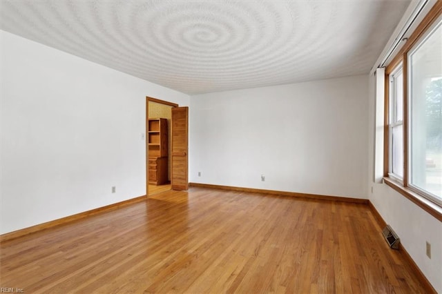 spare room featuring baseboards, visible vents, and light wood finished floors