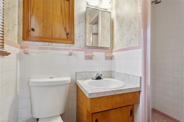 full bath with wallpapered walls, toilet, wainscoting, tiled shower, and vanity