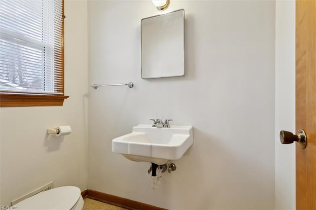 half bathroom featuring toilet, baseboards, and a sink