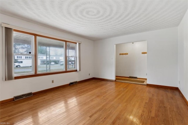 unfurnished room featuring visible vents, light wood-style flooring, and baseboards