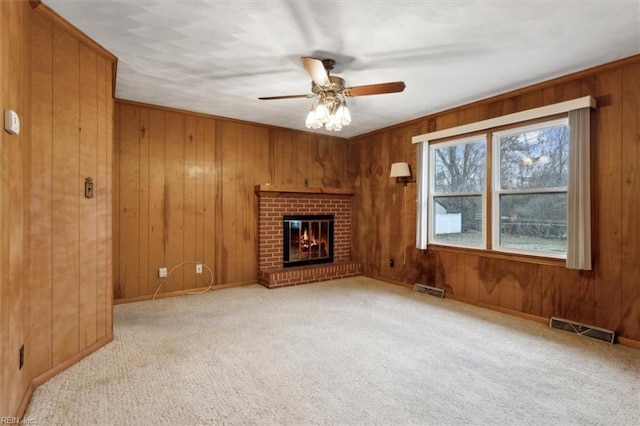 unfurnished living room with ceiling fan, visible vents, carpet floors, and wood walls