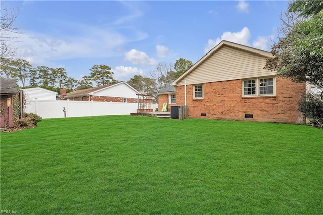 rear view of house with a deck, brick siding, fence, crawl space, and a lawn