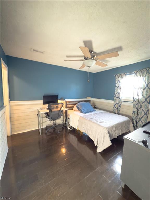 bedroom featuring a ceiling fan, visible vents, a textured ceiling, and wainscoting