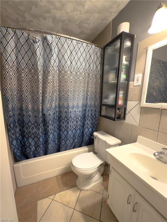 full bathroom with toilet, tile patterned floors, shower / bathtub combination with curtain, vanity, and tile walls