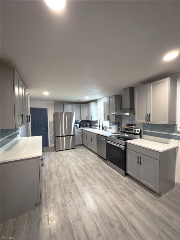 kitchen featuring decorative backsplash, wall chimney exhaust hood, appliances with stainless steel finishes, light countertops, and gray cabinetry