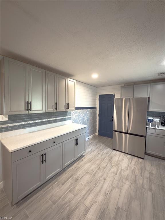 kitchen featuring gray cabinets, light countertops, freestanding refrigerator, a textured ceiling, and light wood-type flooring