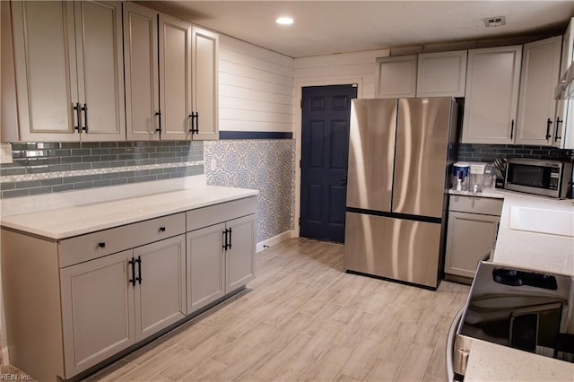 kitchen featuring recessed lighting, backsplash, light wood-style flooring, gray cabinetry, and appliances with stainless steel finishes