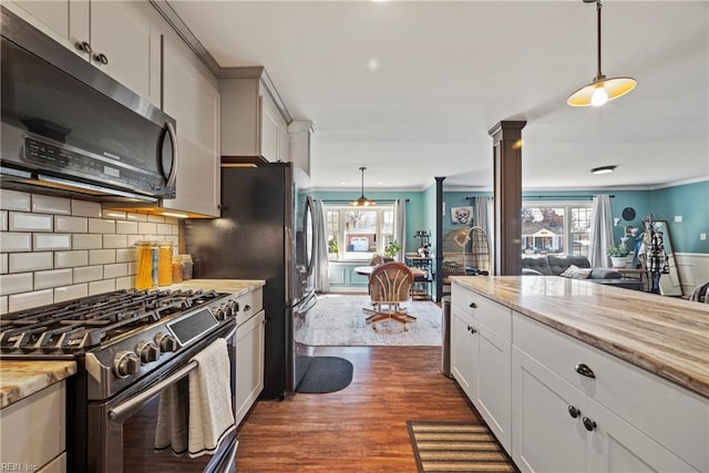 kitchen with dark wood-style flooring, decorative light fixtures, backsplash, appliances with stainless steel finishes, and ornate columns