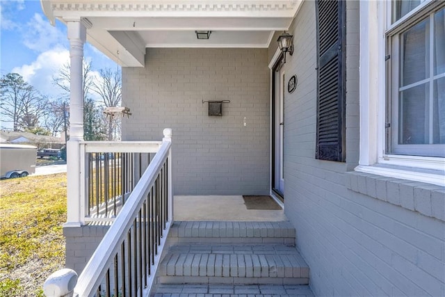 view of exterior entry with a porch and brick siding