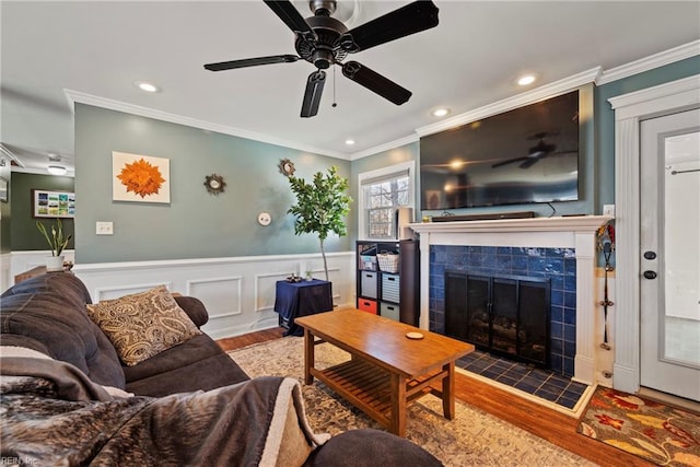 living area featuring wainscoting, crown molding, a tiled fireplace, and wood finished floors