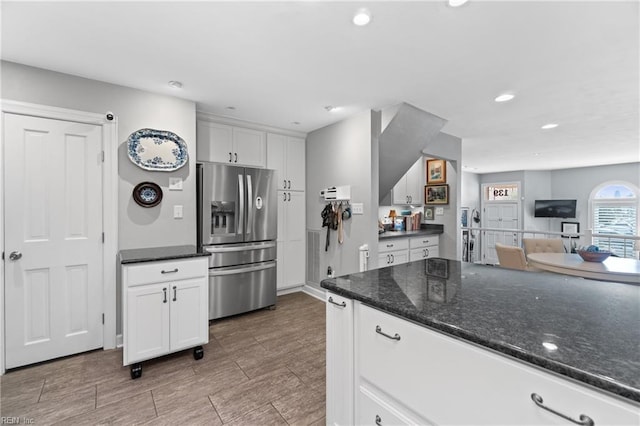 kitchen with stainless steel fridge, dark stone counters, white cabinets, open floor plan, and recessed lighting