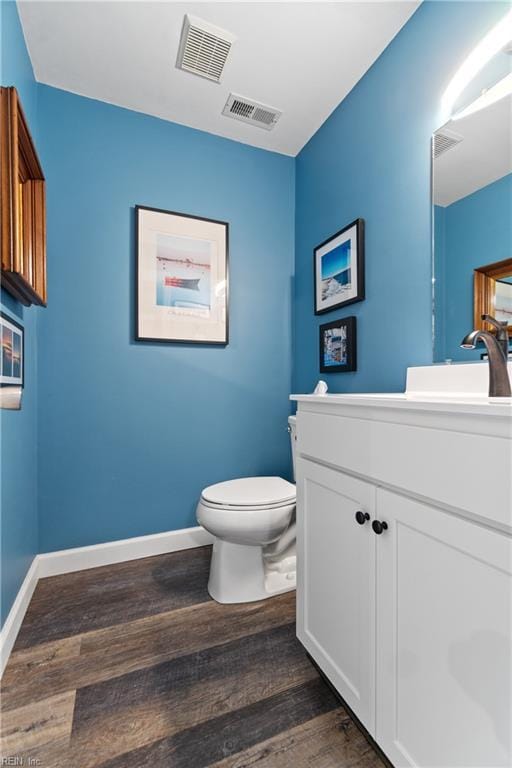 half bathroom featuring visible vents, vanity, toilet, and wood finished floors