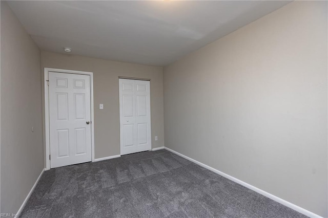 unfurnished bedroom with a closet, dark carpet, and baseboards