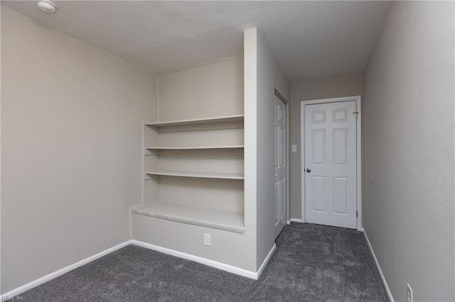 corridor featuring dark carpet and baseboards