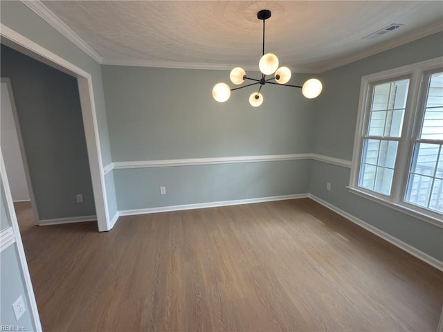 spare room featuring a notable chandelier, visible vents, dark wood-type flooring, ornamental molding, and baseboards