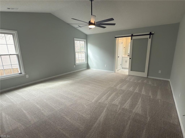 unfurnished room with lofted ceiling, a barn door, light colored carpet, a ceiling fan, and visible vents