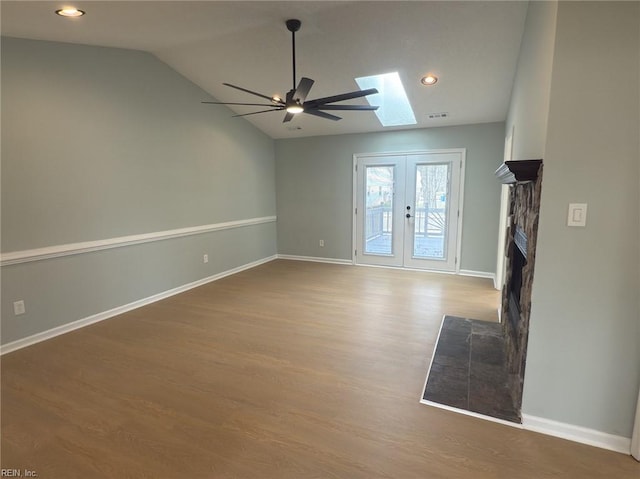 unfurnished living room featuring a fireplace, lofted ceiling with skylight, ceiling fan, wood finished floors, and baseboards