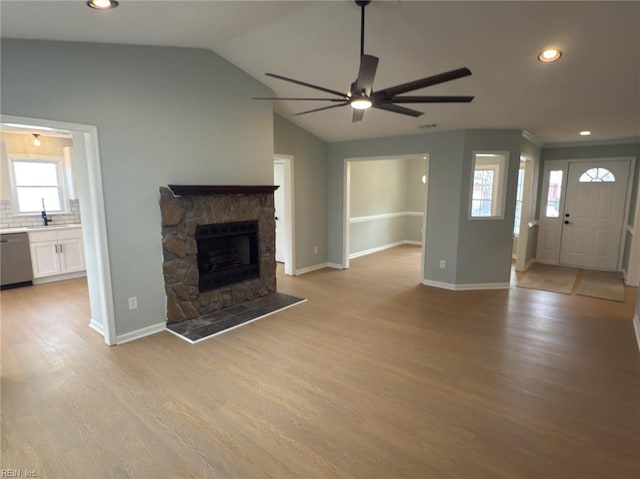 unfurnished living room with lofted ceiling, a stone fireplace, light wood-style flooring, a ceiling fan, and baseboards